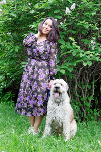 Portrait of woman with dog on grass against plants