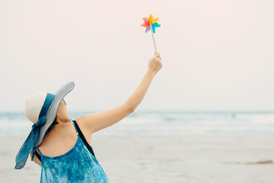 Rear view of woman holding pinwheel toy at beach against sky