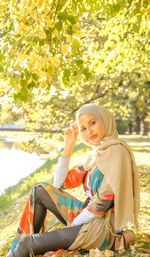 Side view of smiling young woman sitting by lake