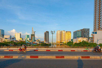 People on road by buildings against sky in city