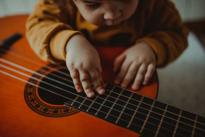 Midsection of child playing guitar at home