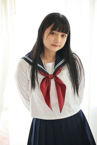 Portrait of young woman standing against curtain