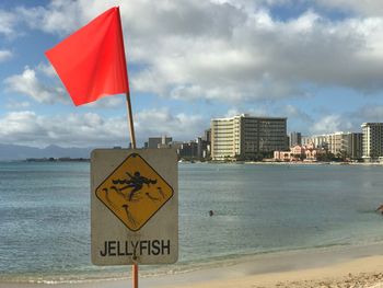 Warning sign on beach against sky in city