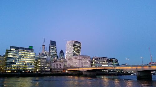 Bridge over river by buildings against clear blue sky