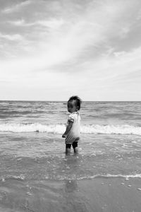 Rear view of woman standing at beach against sky