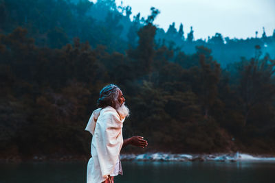 Side view of woman standing by lake against trees