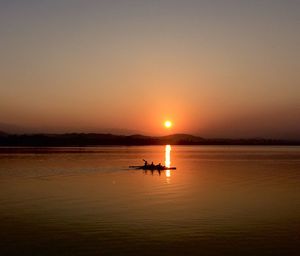 Silhouette people sailing on sea against clear sky during sunset