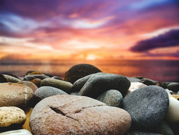 Stones on rocks at beach against sky during sunset
