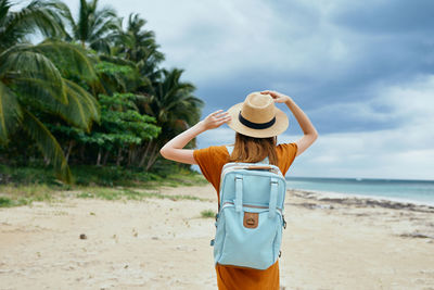 Rear view of woman standing at beach against sky