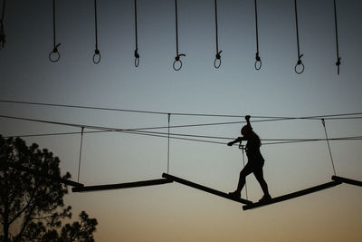 Low angle view of silhouette girl walking on rope against sky