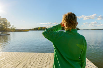 Rear view of woman standing by lake against sky