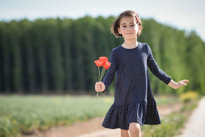 Portrait of girl holding flowers on field
