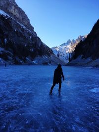 Rear view of woman ice skating by snowcapped mountain against sky