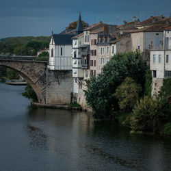 Arch bridge over river by buildings against sky