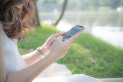 Midsection of woman using mobile phone while sitting on grass