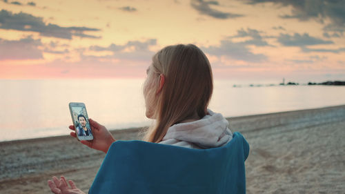 Rear view of woman using mobile phone at beach