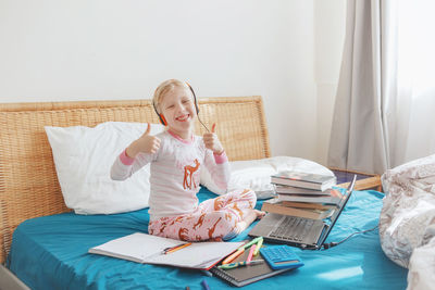 Portrait of smiling girl showing thumbs up while studying on bed at home