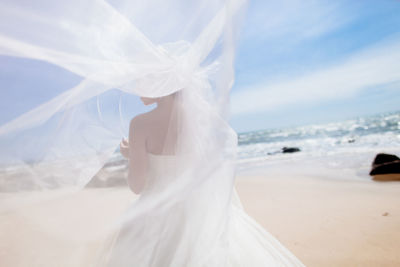 Rear view of bride in dress standing at beach