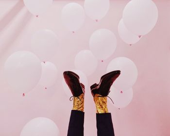 Low section of man with balloons against pink wall during party