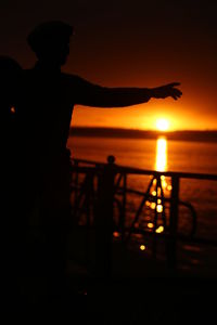 Silhouette people standing by railing against sea during sunset