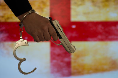 Cropped hand of male criminal holding gun against british flag