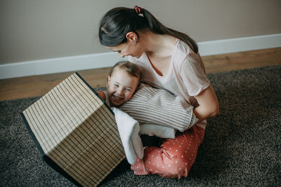  mother in a home suit is sitting at home on the floor her daughter climbed into the laundry basket