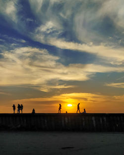 Silhouette people on beach against sky during sunset