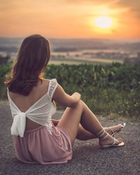 Rear view of woman sitting against sea during sunset