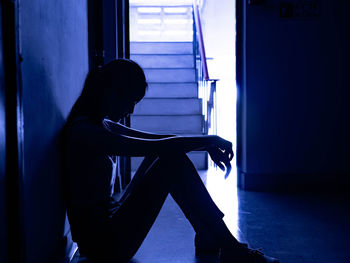 Side view of silhouette woman sitting against wall at home