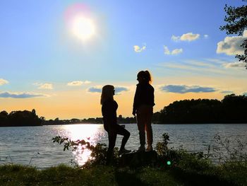 Silhouette woman standing by lake against sky during sunset