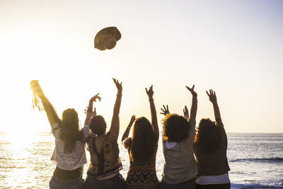 People enjoying at beach against sky during sunset