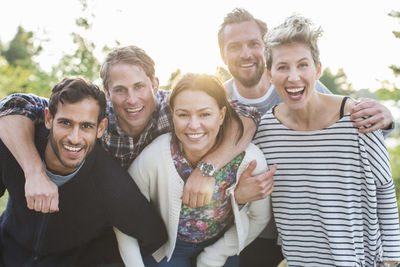 Group portrait of happy friends enjoying picnic at lakeshore