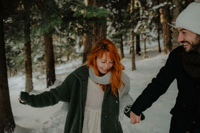 Smiling couple holding hands walking on snow covered land in forest