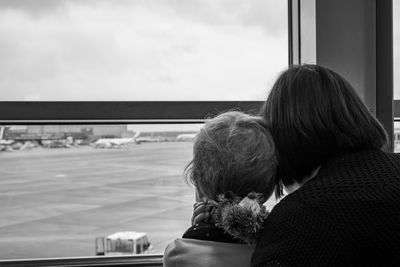 Rear view of mother with son looking at runway through glass at airport