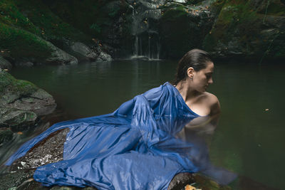 Young woman standing in lake against waterfall