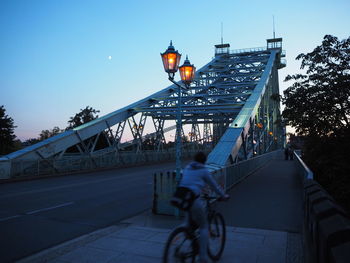 People riding bicycle on bridge against sky in city