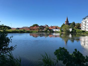 Scenic view of river by buildings against clear blue sky