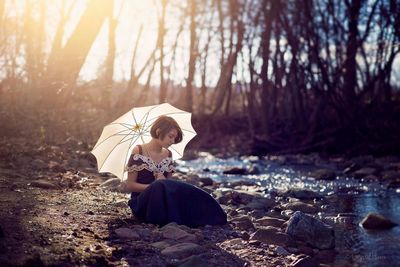 Woman sitting by stream in forest