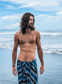 Full length of shirtless man standing at beach against sky