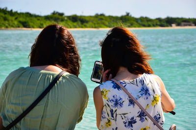 Rear view of friends looking at smart phone by sea