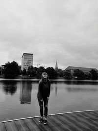 Portrait of smiling young woman standing on jetty over lake against cloudy sky