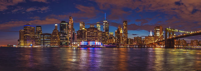 Illuminated bridge over river against buildings at night