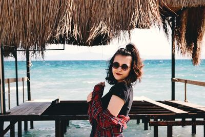 Portrait of smiling young woman standing in shed against sea at beach