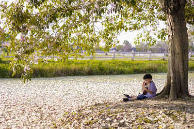 Side view of cute boy playing guitar against tree at park