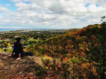 Woman sitting towards mountain against sky during autumn