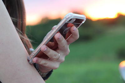 Close-up of hand holding smart phone during sunset