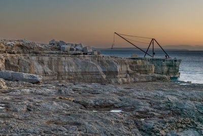 Rocks by sea against sky during sunrise