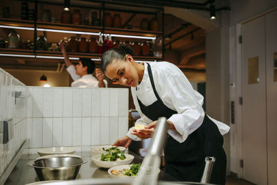 Female chef holding lemon slice while garnishing salad at commercial kitchen in restaurant