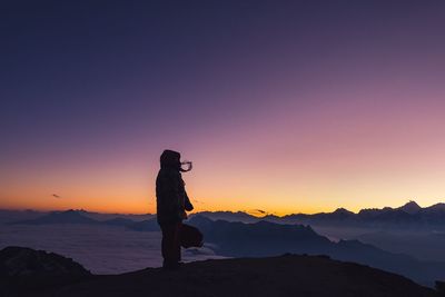 Silhouette person standing on mountain against sky during sunset