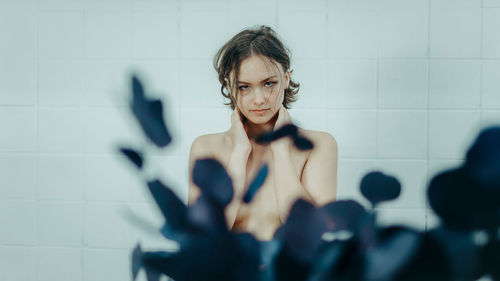 Portrait of young woman standing against wall